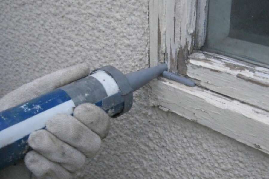 A gloved hand pressing sealant into a gap at the edge of a wall