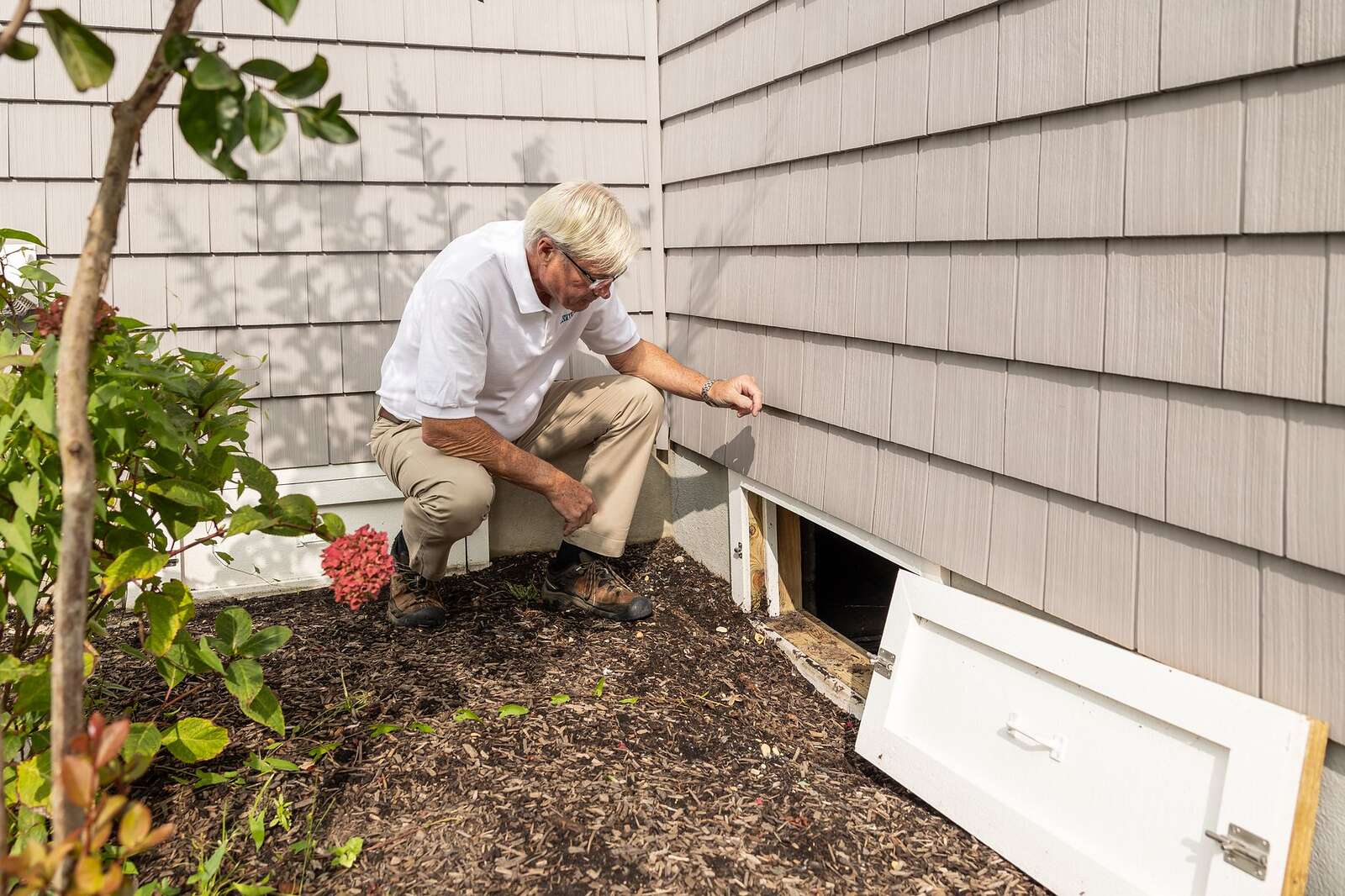 A person crouched at a foundation vent on the side of a raised-foundation house