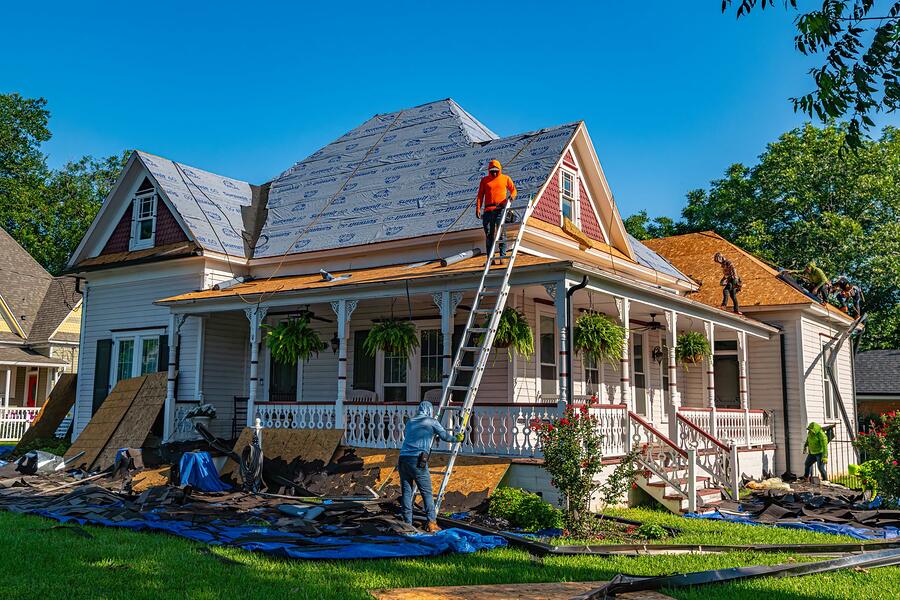 Two workers on ladders at the eave of an older wood-frame house, seen from the driveway