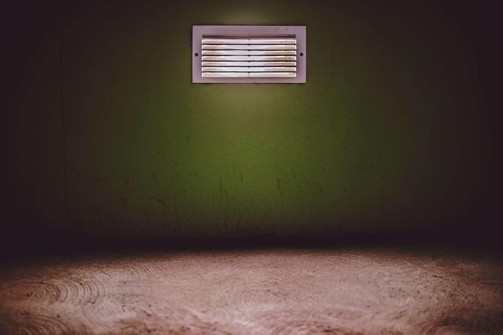 A wall vent in a dim room, where an odor is traced back to a cavity