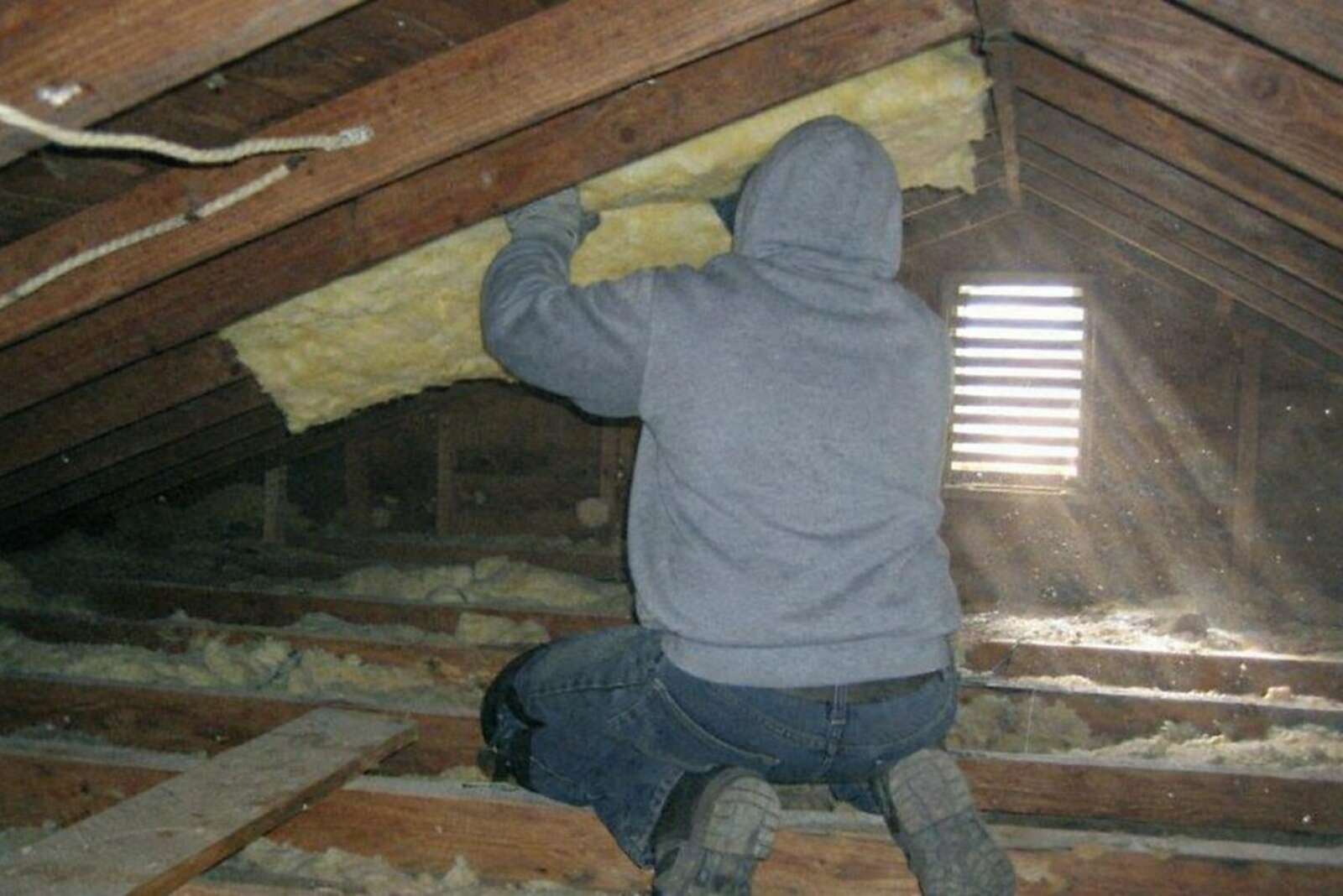 A worker fitting insulation between ceiling joists in an attic